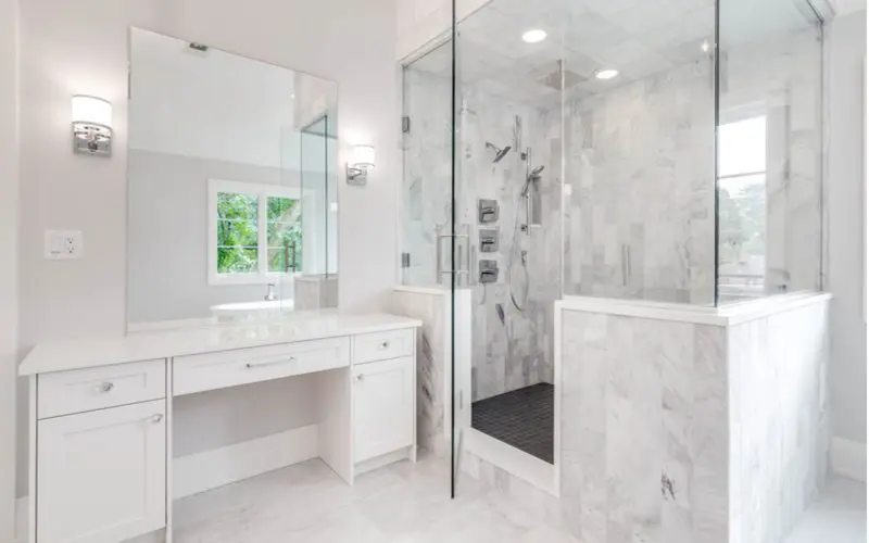 Half-wall walk in shower idea with grey tile and a nice white vanity with a white dressing area in front of a mirror