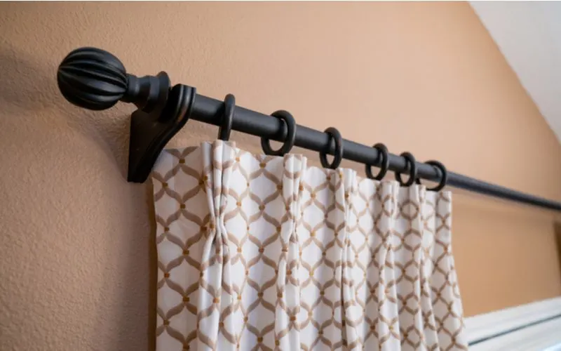 Standard size oil rubbed bronze tension rod holding up decorative curtains in a standard size on a brown wall