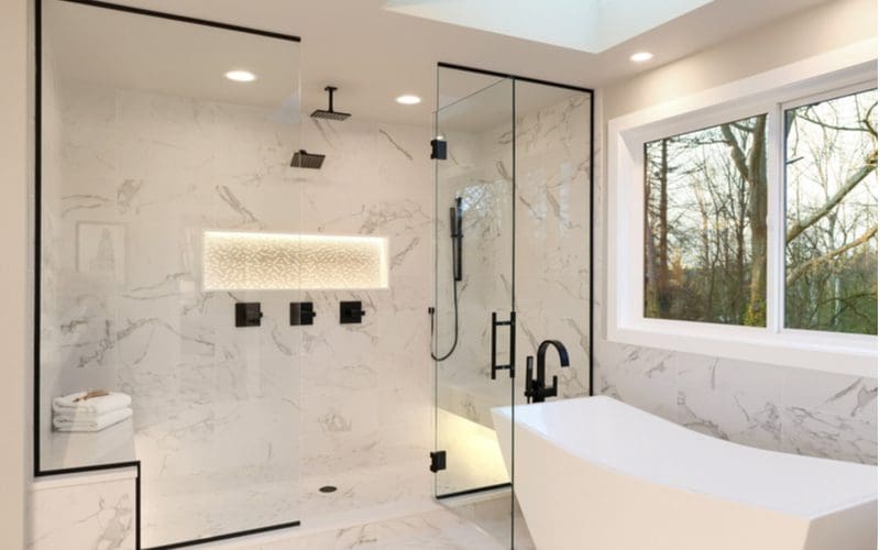 Classic marble tile shower idea with two benches, underlights, a fully-lit soap shelf, and two rain shower heads