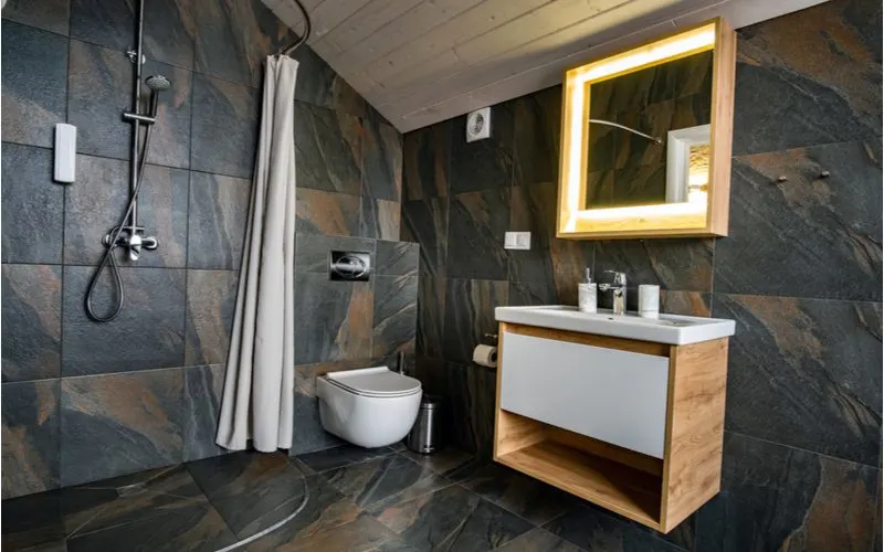 Walk in shower idea with brown slate tile and a wall-mounted vanity with a euro-style toilet next to the open curtain-enclosed shower