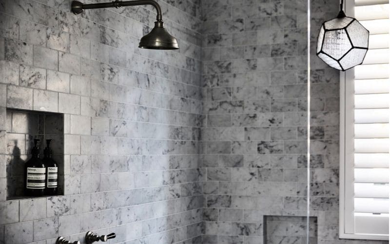 Grey subway tile shower idea with dark bronze fixtures and soap shelf