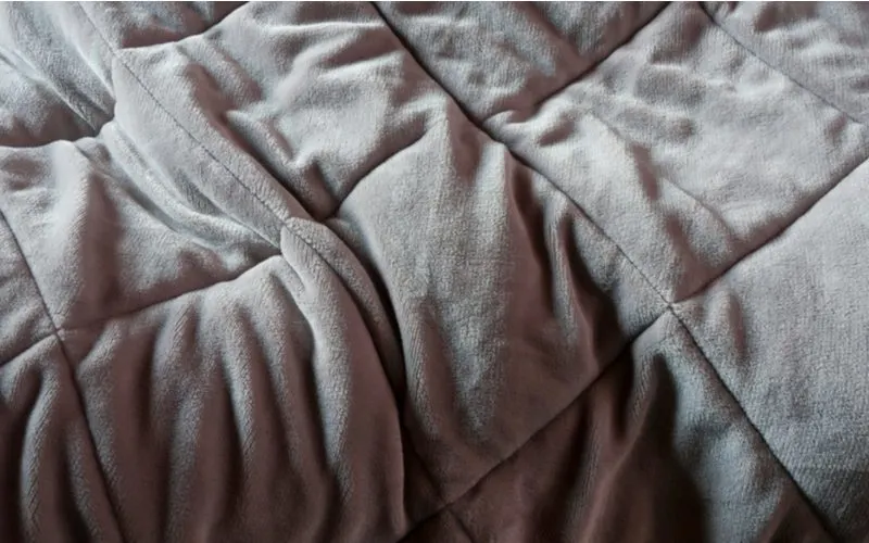 Weighted type of blanket laid out on a bed in grey color and slightly wrinkled