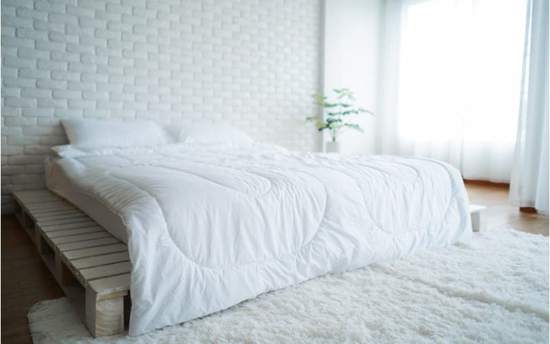 Comforter (a popular type of blanket) laid out on a bed built out of wooden pallets in a brick room