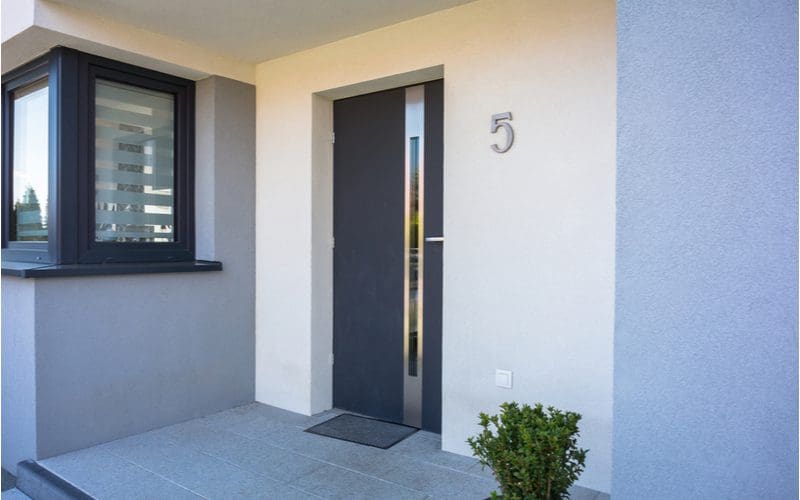 For a piece on grey house ideas, the entryway to a modern stucco home with a metal door with a thin window running down the middle