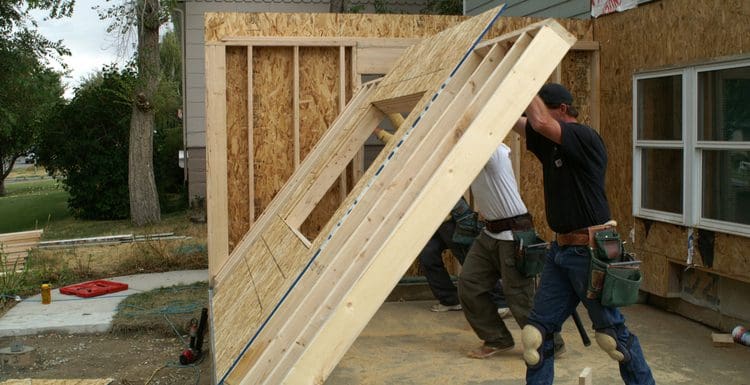For a piece on how much does it cost to add a bedroom to a house, two guys lifting a wooden framed wall as part of an addition