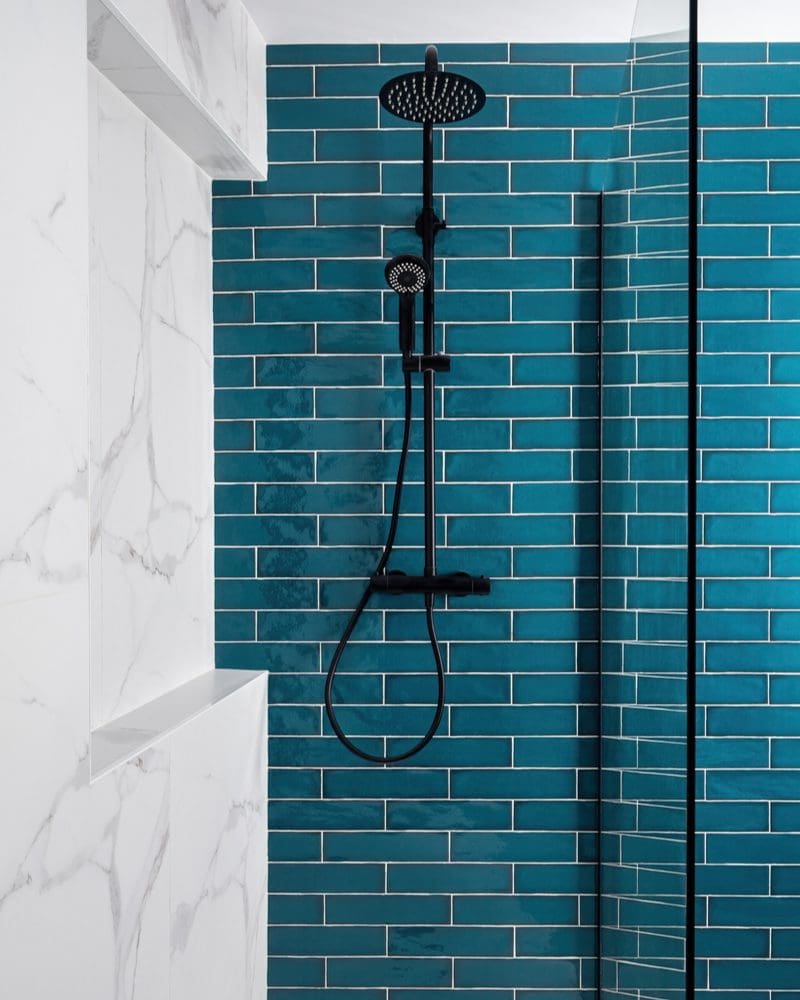 Tile shower idea with a blue subway tile accent wall on one side, a white marble shower surround on the other, and a doorless glass panel on the third wall