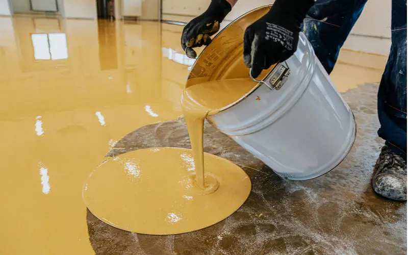 Guy pouring epoxy (great basement flooring idea) onto a bare concrete floor