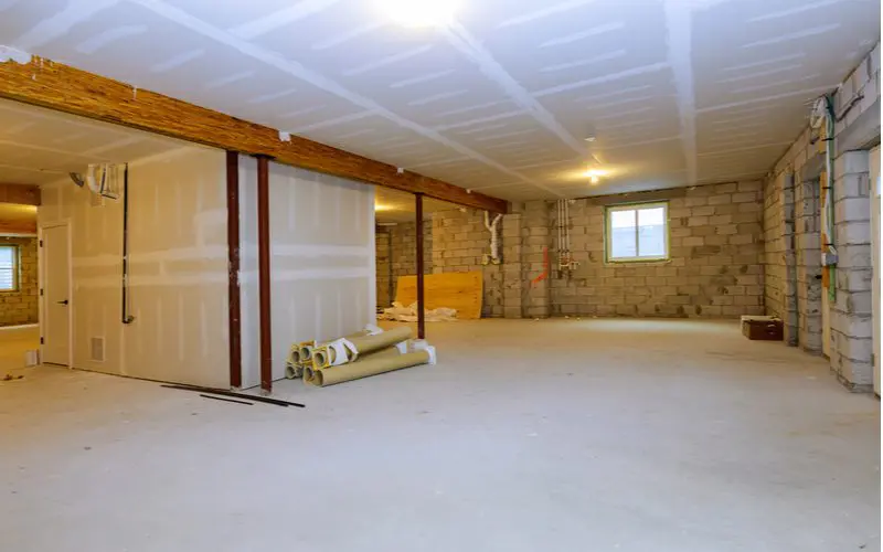 Semi-finished basement with cement floors and brick wall with unfinished drywall and carpet rolls on the floor