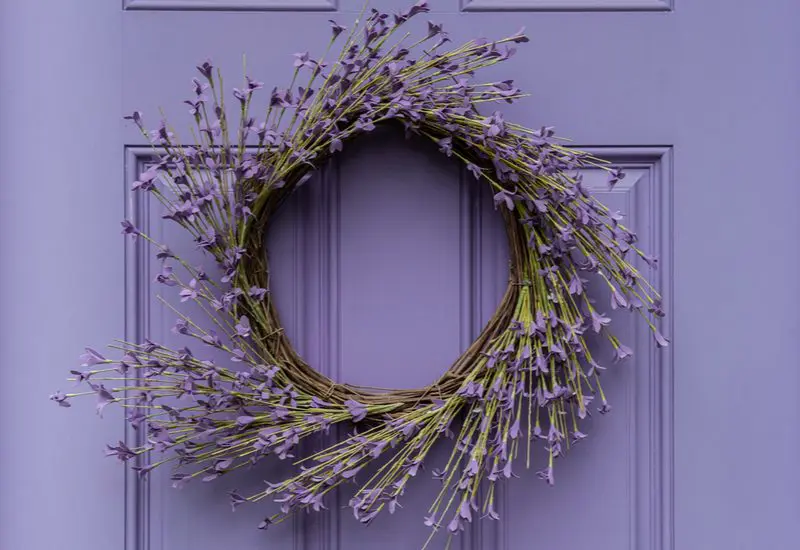 Image for a piece on the best front door colors for tan house showing a close-up of a lavender painted door with a round wooden lilac wreath