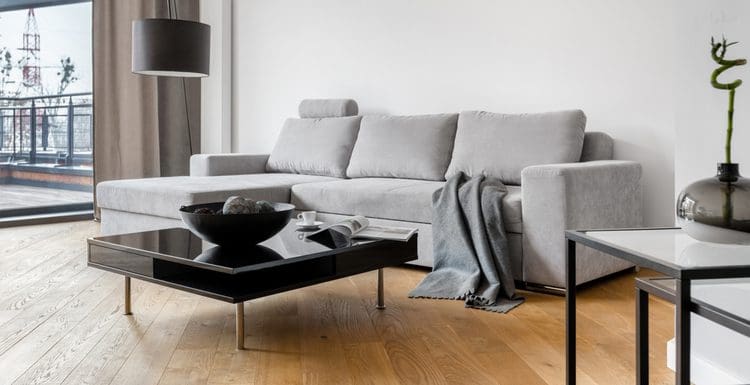 Featured image for a piece on grey couch living room ideas with a brown hardwood floor and white walls