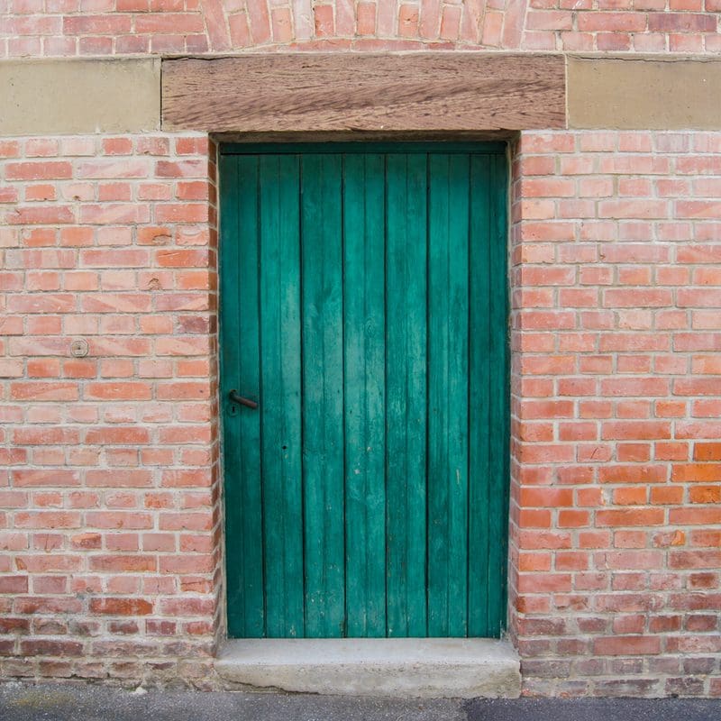 As an idea for a piece titled Front Door Colors for Red Brick House, an emerald green door framed by a simple red brick wall with a single concrete step below