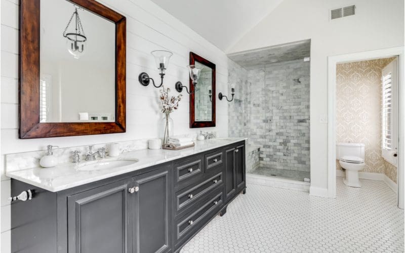 Luxurious bathroom with white terrazzo floor tile, a grey vanity, and grey tile in the shower surround and white shiplap running horizontally across the wall behind the vanity