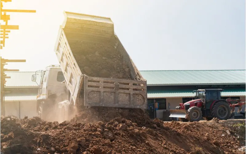 Dump truck pouring a bunch of fill dirt into a pile from the back of its bed