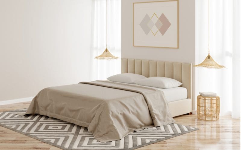 To illustrate what size rug you should put under a king bed, a striped horizontal pattern rug in grey and white coloring below the bed