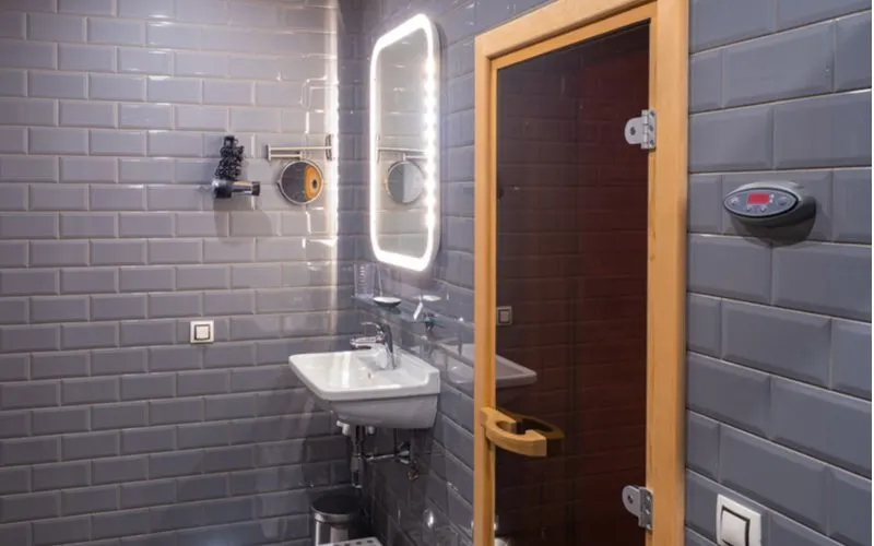 Very unique grey tile bathroom idea featuring beveled subway tile covering the every wall from floor to ceiling and natural oak frame mirror