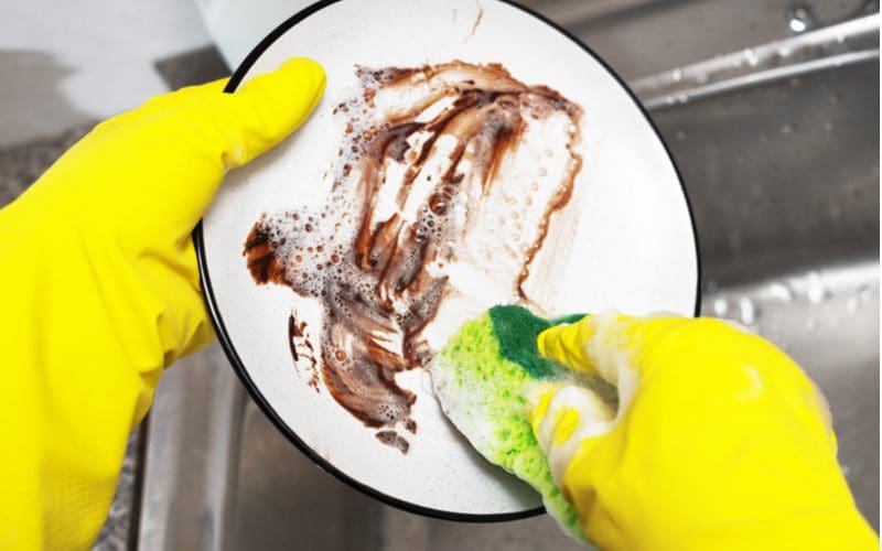 Yellow gloves and a sponge wash dirty dishes that are attracting fruit flies