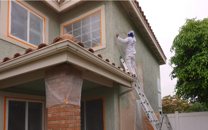 For a piece on types of siding, a guy on a ladder paints a home with stucco exterior on a cloudy day