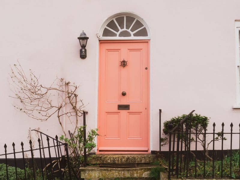 For a piece on the best front door colors for red brick house, a peach-colored door is pictured on a white stucco house