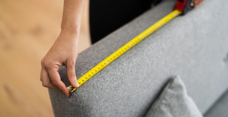 For a piece on standard sofa dimensions, a person with a yellow tape measure determining the length of the arm