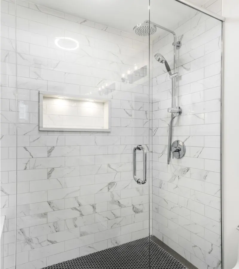 Luxury tile shower idea with white marble subway tile surrounding three walls, a glass wall and door, and a black hexagonal tiled floor