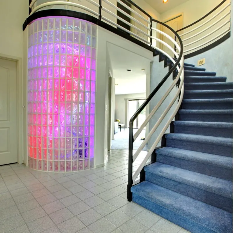 Piece on stair railing ideas featuring blue carpet with a curved staircase next to a glass curved wall