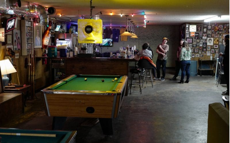 Game room style basement bar idea with lots of felt pool tables next to a group of youths conversing