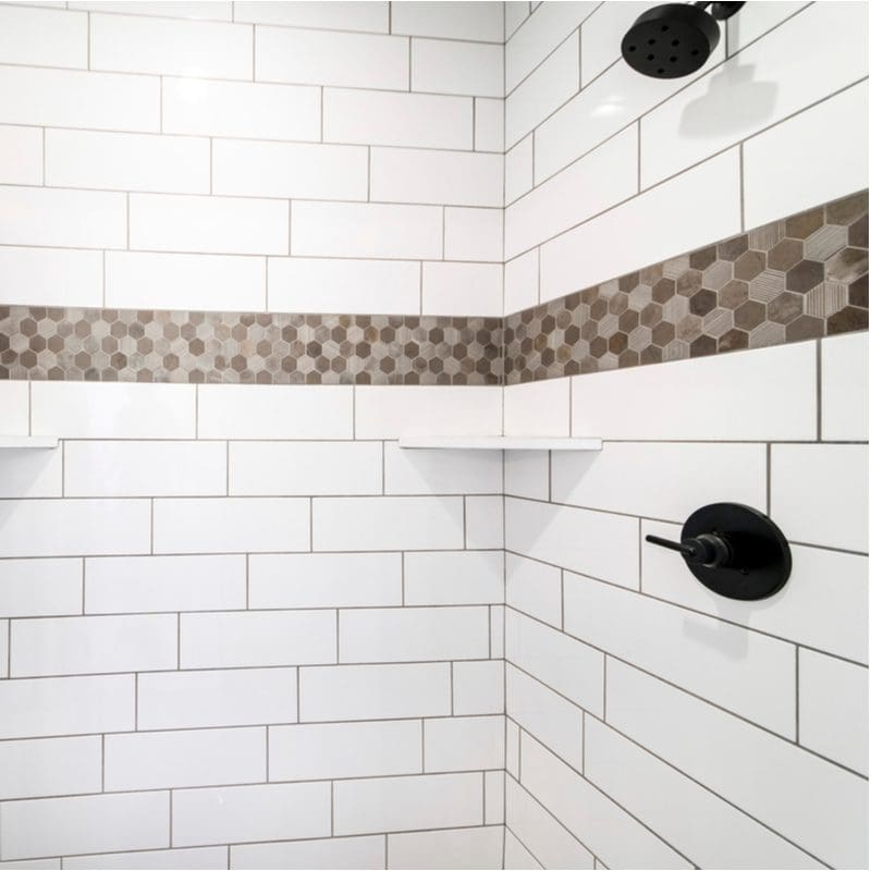 White subway tile shower surround with a brown mosaic tile strip between the shower head and the faucet