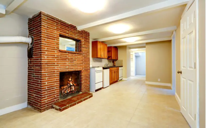 Empty warm basement idea with a brick wood fireplace in the middle of a kitchen with ceramic tile flooring