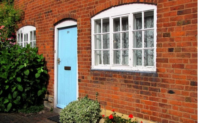 Sky blue colored front door on a red brick house next to a white painted three-panel window