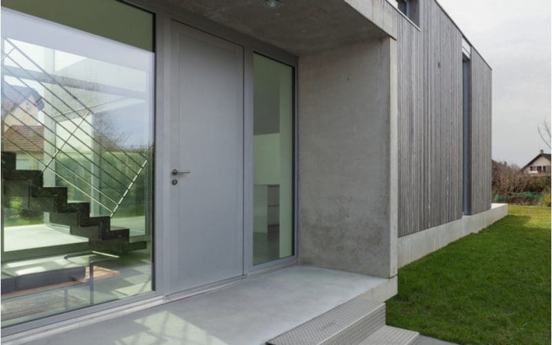Concrete house entrance idea showing a modern staircase with metal railing through the big window on the left
