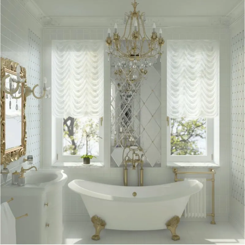 White clawfoot tub in a white room with two large windows on either side of the tub below a glass and gold chandelier