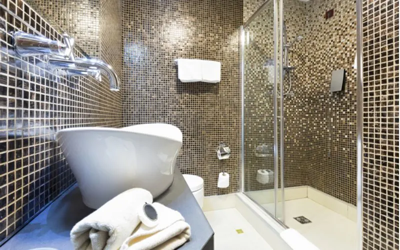Tile shower idea that ties in black and gold mini square tiles on every wall, including the shower surround and behind the sink and toilet