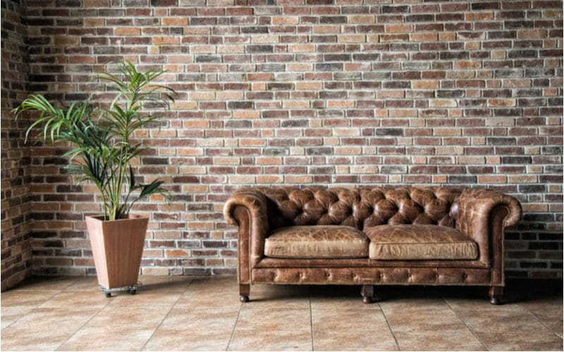 Brick wall with a dark brown leather couch in a living room with tan ceramic tile