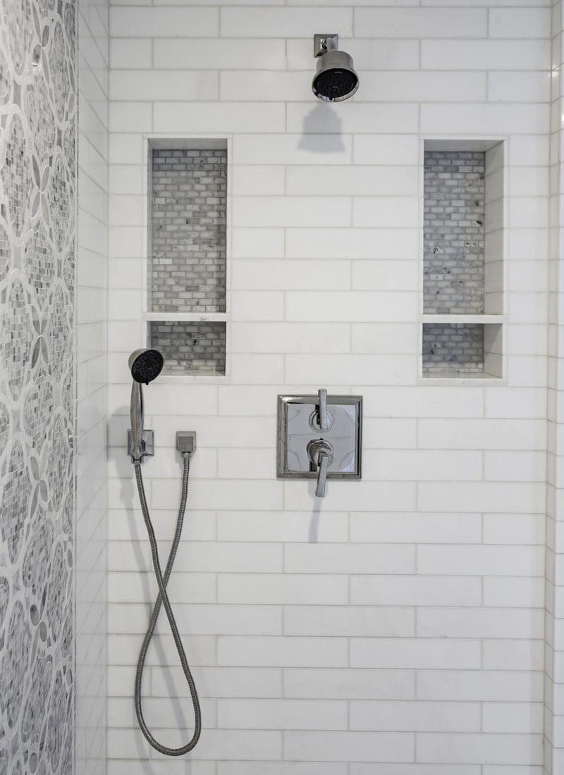 As an example of the best tile shower ideas, a subway tile shower with two large soap shelves on either side of the head and faucet with a spanish-style grey tile accent wall