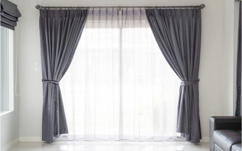 Image for a piece on curtain sizes featuring a big window in the front of a house with grey curtains draped on either size