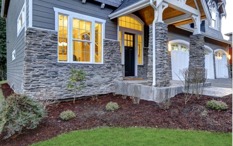House with stone siding and nice mulch landscape beds with its lights on at dusk