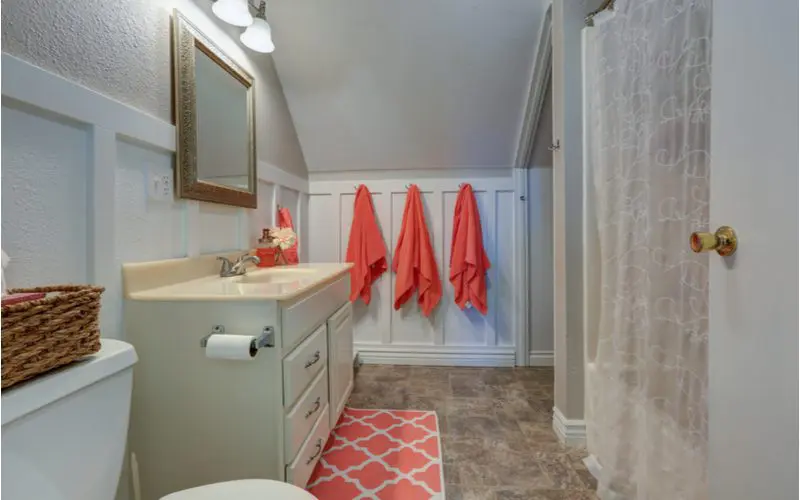 White bathroom wainscoting idea with salmon bathroom towels hanging from the drywall alongside same color floormat