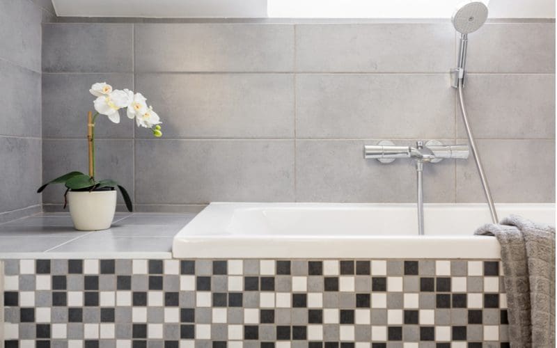 Grey tile bathroom idea featuring glass mosaic tile on the front of the tub and simple 2 x 4 grey tiles on the tub surround