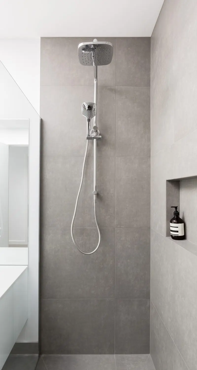 Small walk in shower idea with a rain showerhead and grey tile next to a small vanity