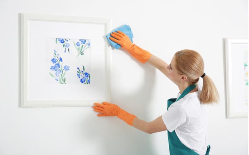 Woman cleaning an eggshell paint wall with a microfiber towel while wearing an apron