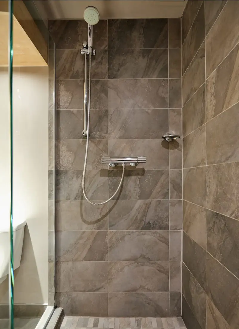 Rain shower head mounted high up on a brown slate tile surround with one glass wall