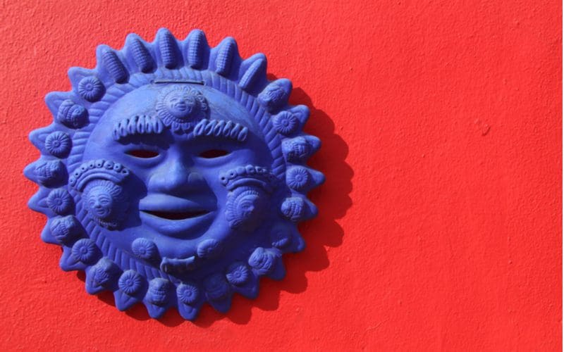 Blue sun handicraft wall decor on a red wall, typically found in Mexican kitchens