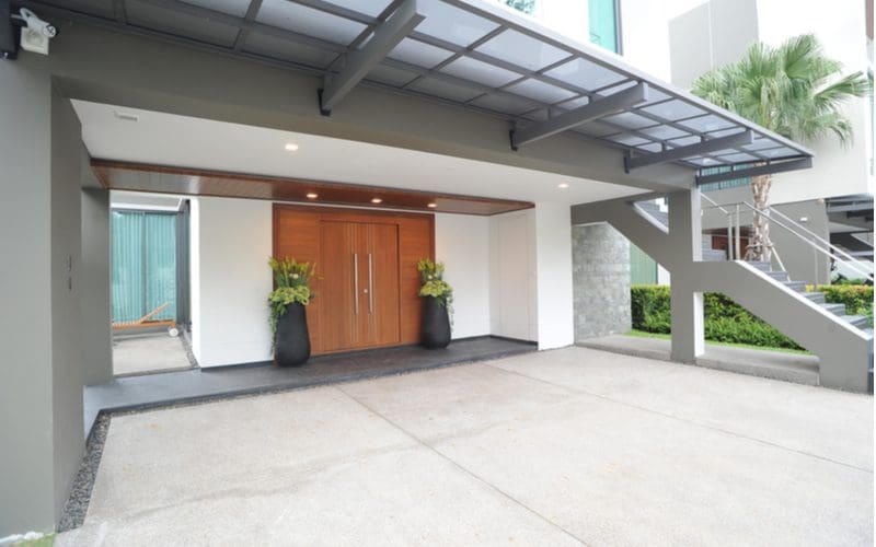 Modern home entrance with a large metal overhang above a simple double-panel wooden door in front of a driveway