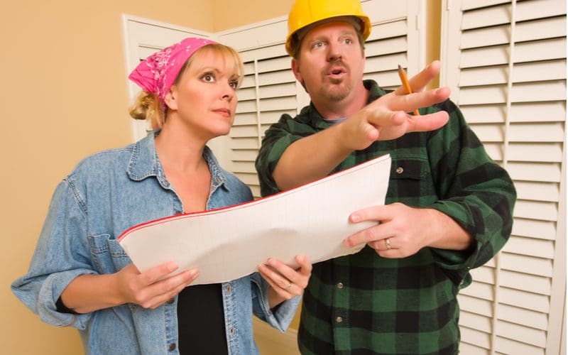 Contractor and woman standing in a bedroom discussing adding a second bedroom while holding a piece of paper blueprints