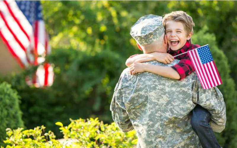 To symbolize what a green porch light means, a veteran in camo fatigues holding a child hugging the dad holding an American flag