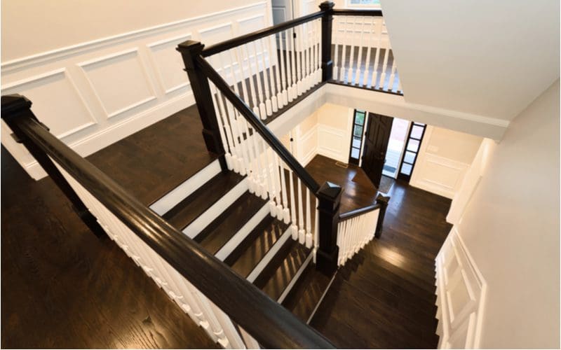 White wainscoting stair trim idea that makes a great contrast to the dark floors and dark handrail supported by white balusters