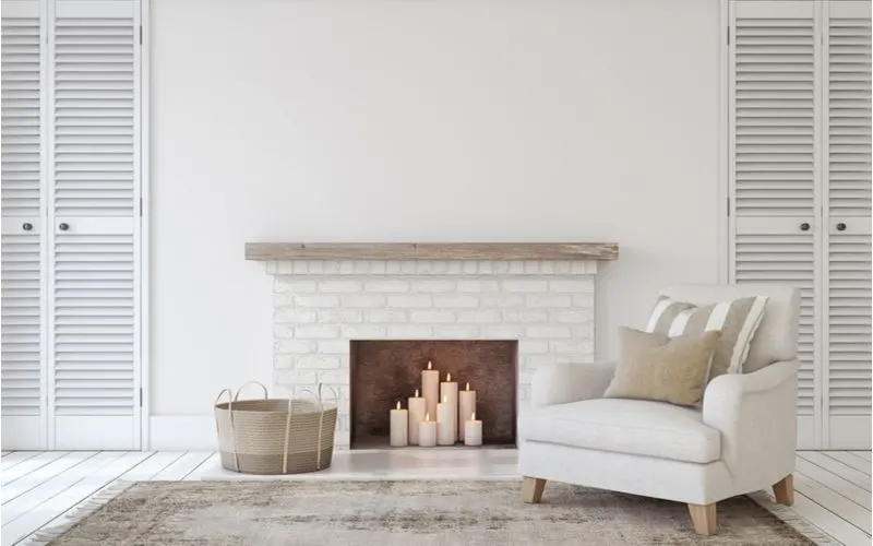 Photo of a living room with a fireplace but instead of a fire there are battery operated candles inside next to a white comfy looking chair