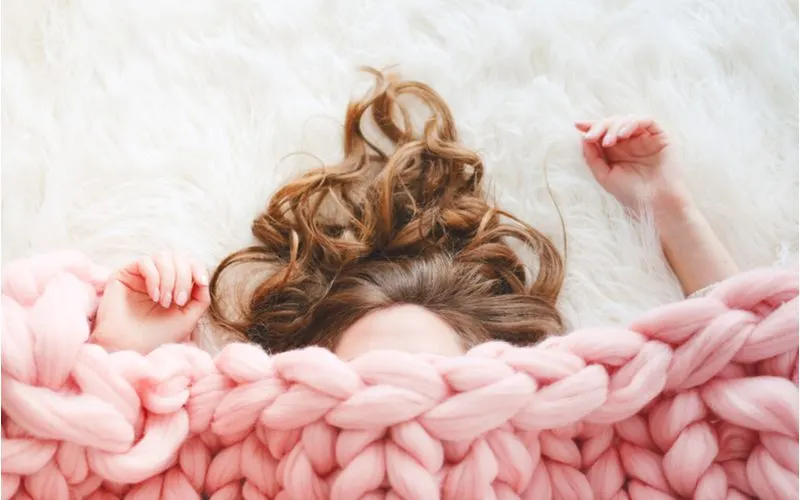 Woman with long brown hair laid out under a braided type of blanket and you can only see her arm and hand and hair