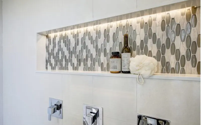 Walk-in tile shower idea with a soap shelf that's lit from above with glass tiles in the background