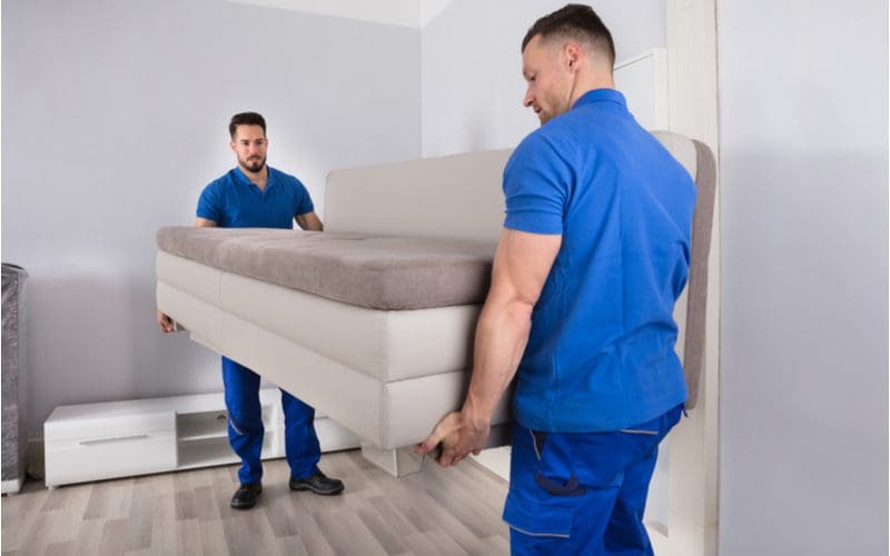Two bulky young men in blue outfits moving a piece of furniture into a living room